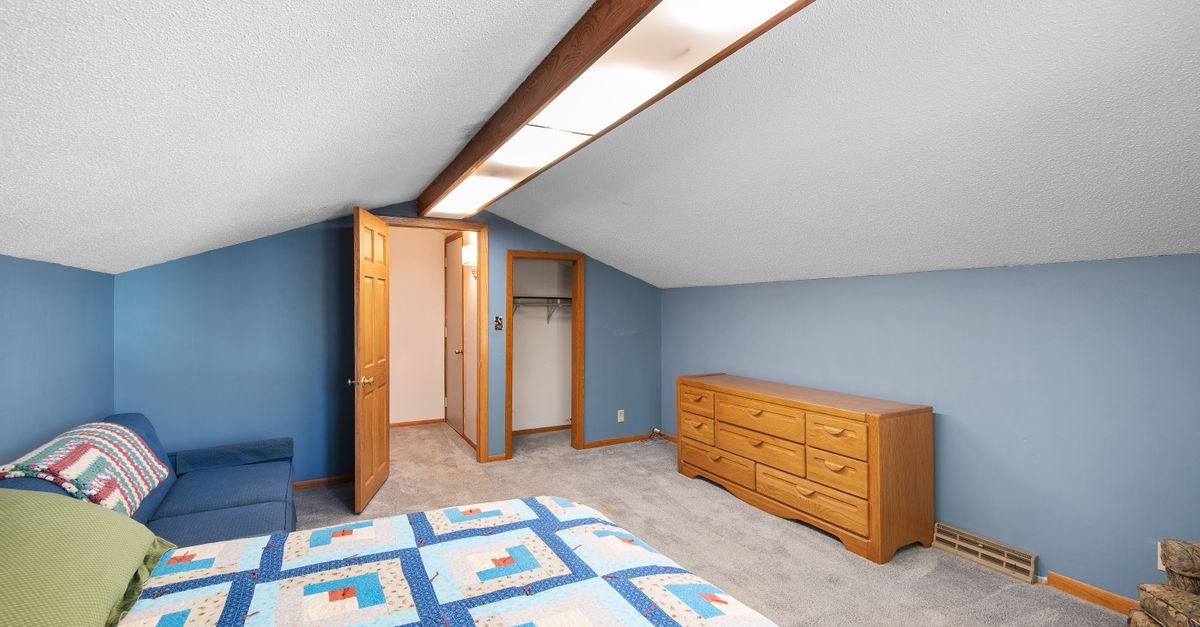 Bright attic bedroom featuring a colorful quilt, wooden dresser, and cozy ambiance.